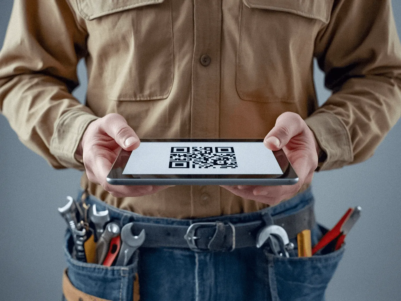 Close-up of a service technician in a tool belt holding a digital tablet displaying a QR code for contactless payment or project details.
