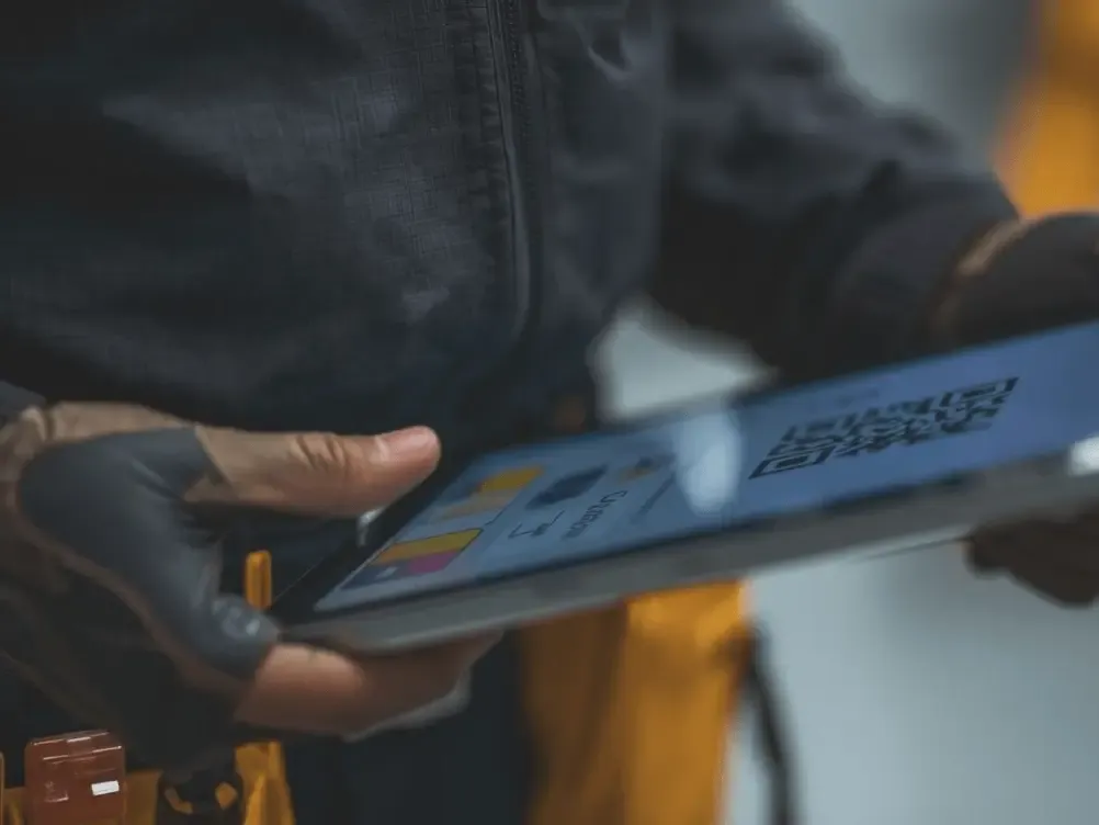 A professional service technician in a brown uniform holding a digital tablet to display a Yelp review QR code for a customer scan.