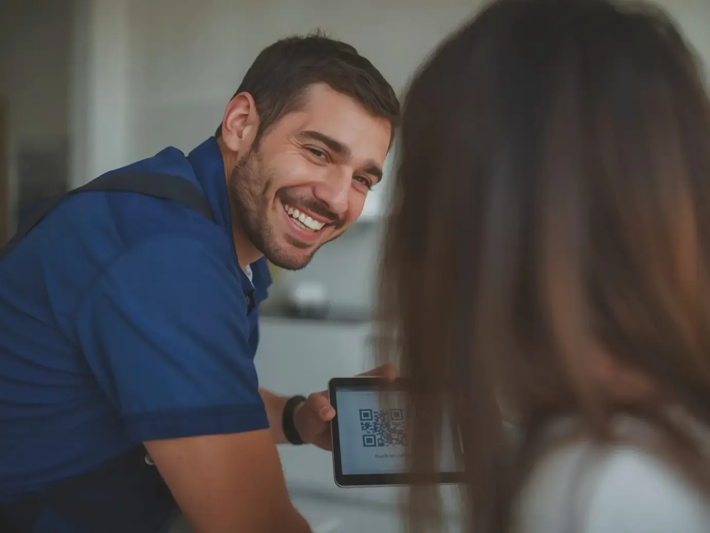 A smiling service technician in a blue uniform showing a QR code on a digital tablet to a customer for an instant business review.